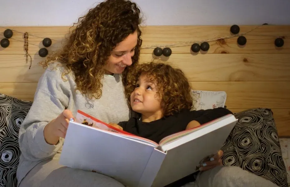 Child looks up lovingly at parent who reads picture book to them at bedtime